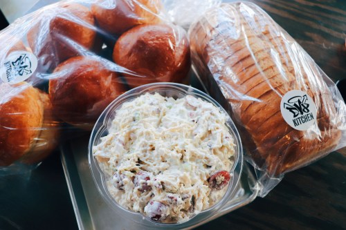 A tray with a container of creamy chicken salad, a loaf of bread, and several rolls, all wrapped in plastic.
