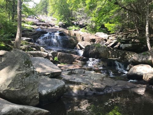 A serene waterfall cascades over large rocks, surrounded by lush greenery and a calm pool of water below.