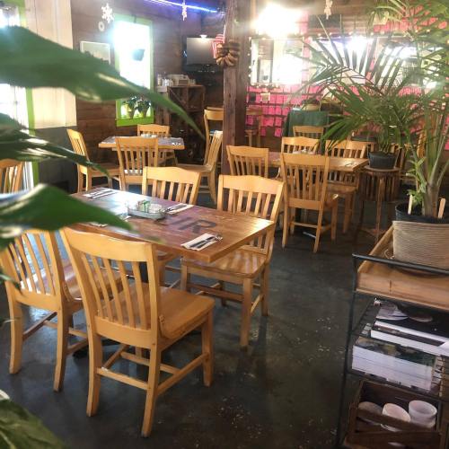 A cozy restaurant interior with wooden tables and chairs, plants, and colorful decor on the walls.