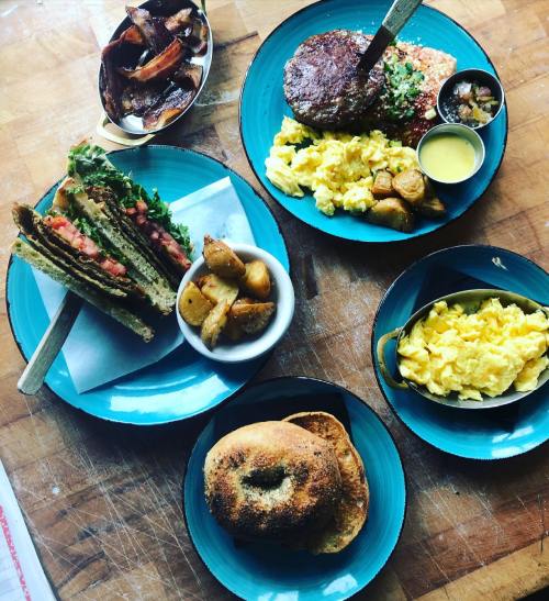 A spread of breakfast dishes including scrambled eggs, a burger, a sandwich, and roasted potatoes on blue plates.