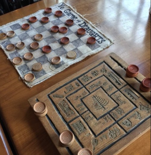 Two vintage board games: a checkers board with pieces and a carved game board with intricate designs and circular pieces.