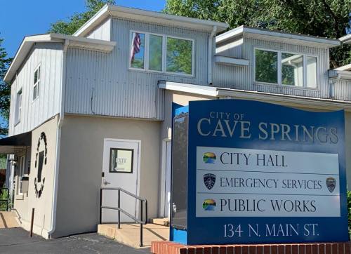 City Hall of Cave Springs, featuring a sign for emergency services and public works, with a flag visible on the building.