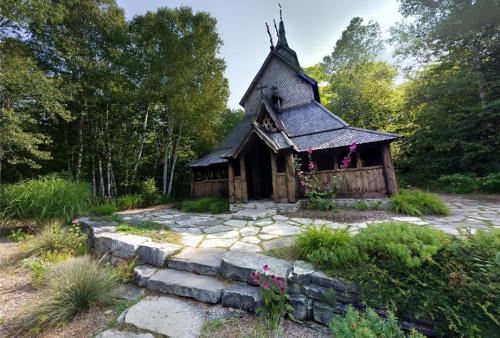 A unique wooden building with a steep roof, surrounded by greenery and stone pathways.