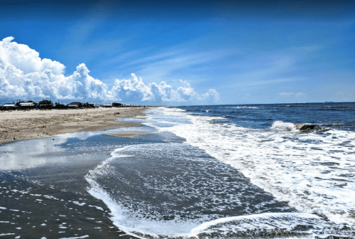 A serene beach scene with gentle waves lapping at the shore under a bright blue sky with fluffy clouds.
