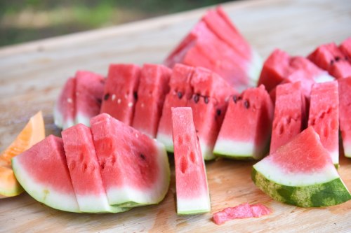 Sliced watermelon pieces arranged on a wooden surface, with a small piece of cantaloupe nearby.