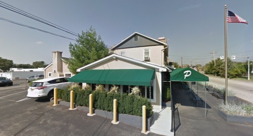 A small restaurant with a green awning, surrounded by plants, and an American flag flying nearby.