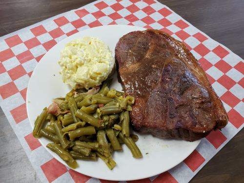A plate with a grilled steak, green beans, and a serving of potato salad on a red and white checkered background.