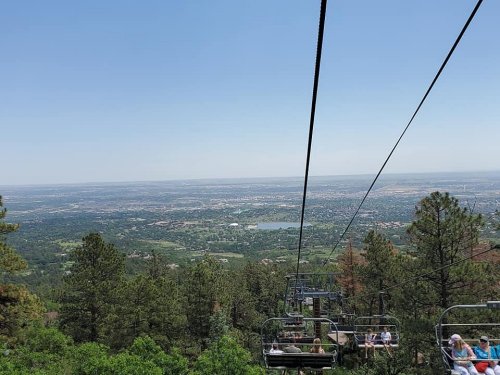 A scenic view from a chairlift, overlooking a lush landscape and distant city under a clear blue sky.