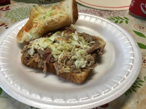 A pulled pork sandwich topped with coleslaw on a paper plate, with a second piece of bread beside it.