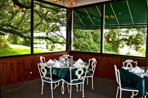 A cozy restaurant interior with green tables, white chairs, and large windows overlooking a lush outdoor view.