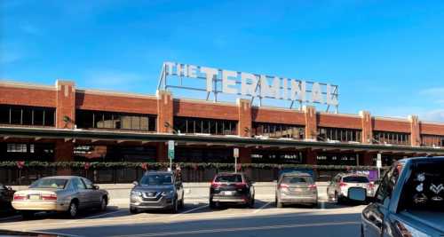 Exterior of a building with a large sign reading "THE TERMINAL," surrounded by parked cars under a clear blue sky.