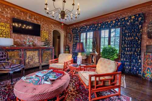 Cozy living room with brick walls, vintage furniture, colorful curtains, and decorative art pieces.