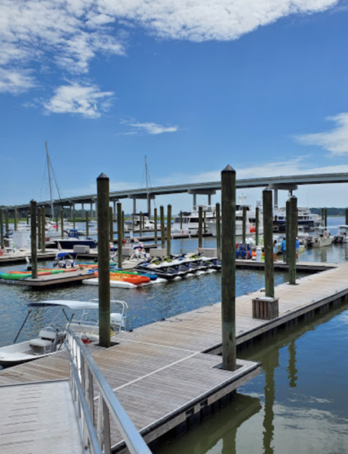 A marina with boats docked, wooden piers, and a clear blue sky with scattered clouds.
