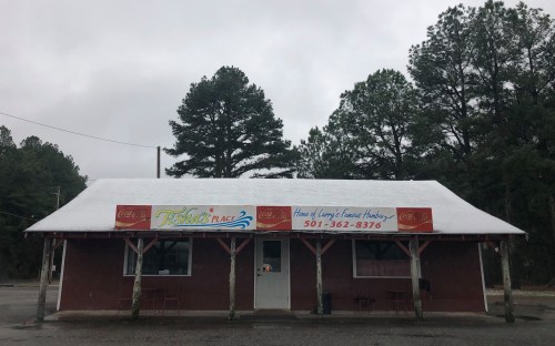 A small, rustic restaurant with a red exterior and a sign reading "Tish's Place" under a cloudy sky.