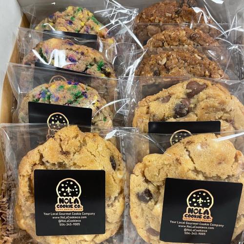A box of assorted cookies in clear packaging, featuring colorful sprinkles and chocolate chips, labeled NOLA Cookie Co.