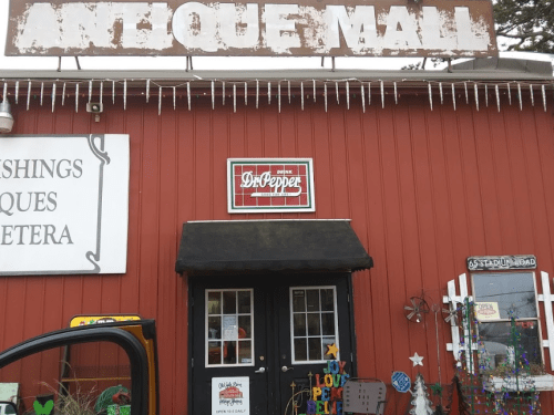 Exterior of an antique mall with a red building, a sign above, and a Dr. Pepper sign on the door.