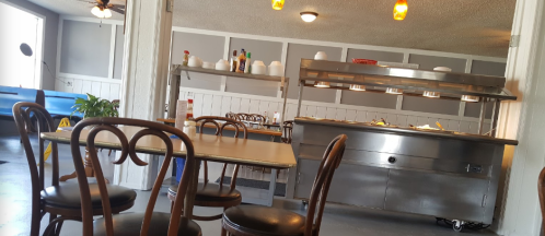 A cozy restaurant interior featuring a table, chairs, and a food serving station with condiments.