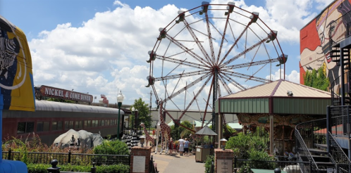 A vibrant amusement park scene featuring a Ferris wheel, carousel, and colorful buildings under a blue sky with clouds.