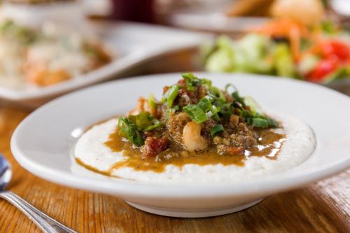 A bowl of creamy grits topped with a savory shrimp and vegetable sauce, garnished with chopped green onions.