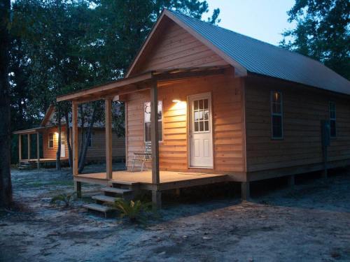A wooden cabin with a porch, lit by a warm light, surrounded by trees at dusk.