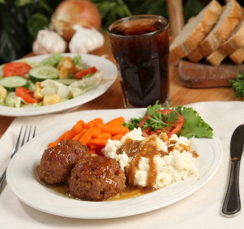 A plate with meatballs, mashed potatoes, carrots, and salad, alongside a glass of cola and slices of bread.