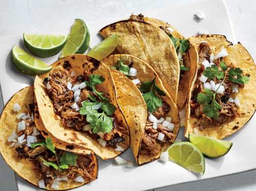 A plate of tacos filled with meat, topped with onions and cilantro, served with lime wedges.