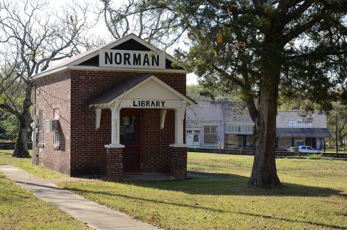A small brick building with a sign reading "Norman Library," surrounded by trees and grass.