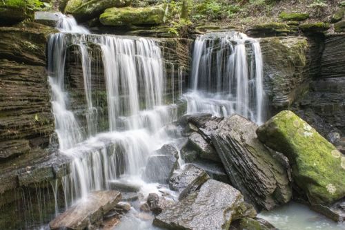 A serene waterfall cascading over moss-covered rocks in a lush, green forest.