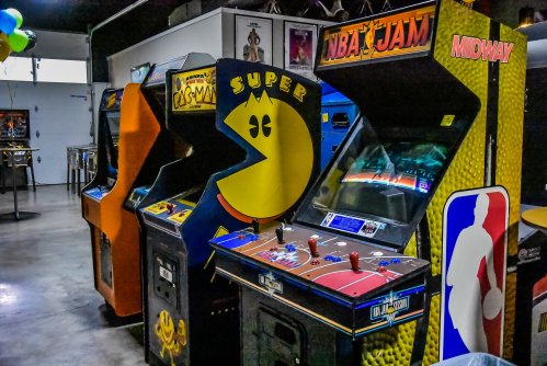 Three vintage arcade machines: Pac-Man, NBA Jam, and another game, set in a retro gaming space.