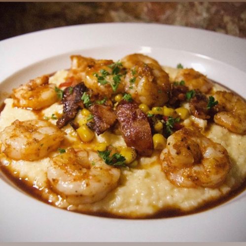 A plate of creamy grits topped with shrimp, bacon, corn, and garnished with parsley.