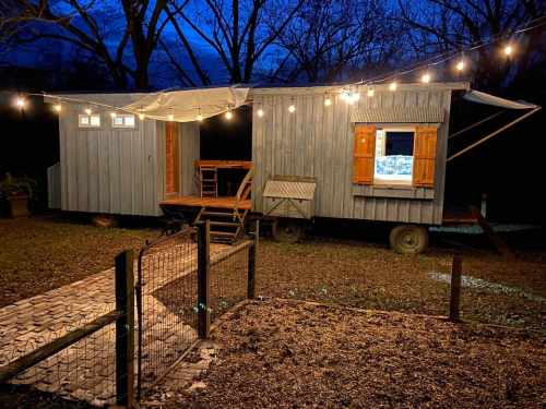 A cozy blue trailer with wooden shutters, illuminated by string lights, set in a dark outdoor space.