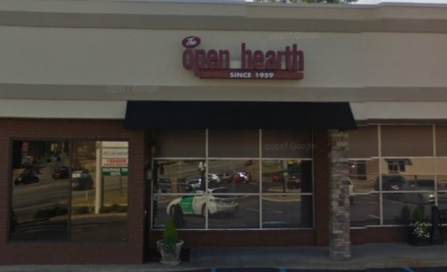 Exterior of a restaurant called "The Open Hearth," featuring a sign and large windows reflecting the street.