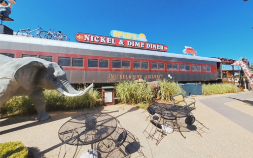 A diner named "Nickel & Dime Diner" with a train car design, surrounded by greenery and outdoor seating.