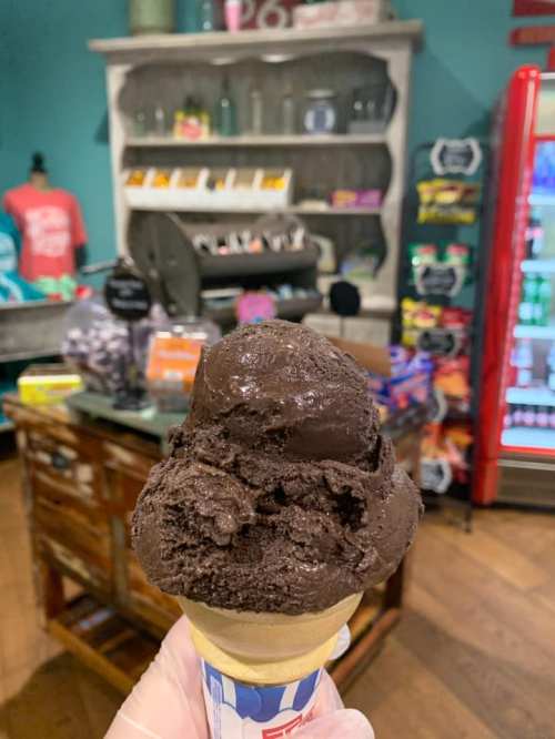 A close-up of a chocolate ice cream cone in a colorful shop with vintage decor and candy displays in the background.