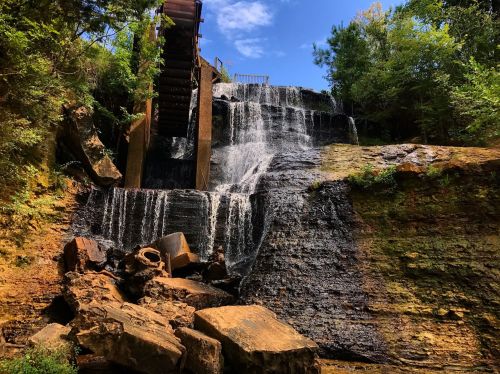A scenic waterfall cascading over rocky terrain, with a wooden structure above and lush greenery surrounding the area.