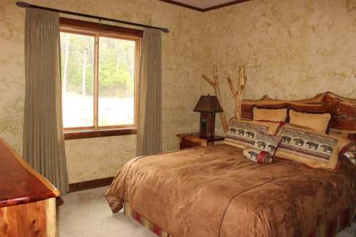 Cozy bedroom with a wooden bed, decorative pillows, and a large window overlooking greenery.