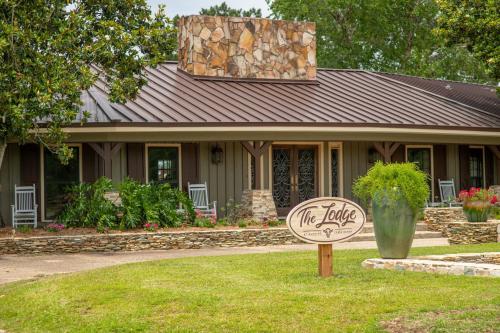 A rustic lodge with a stone facade, rocking chairs, and a sign reading "The Lodge" surrounded by greenery and flowers.