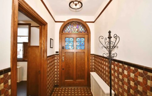 A hallway featuring a wooden door with stained glass, decorative tile walls, and a coat rack.
