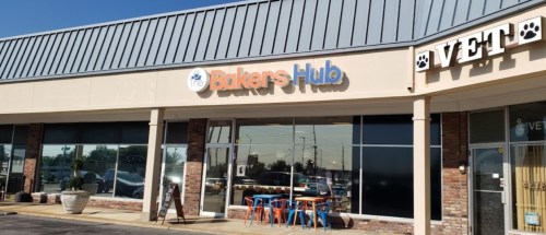 Exterior of a storefront featuring "The Bakers Hub" sign, with colorful outdoor seating and a veterinary clinic nearby.