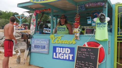 A beach stand with a smiling vendor, offering drinks like Bud Light and Pepsi, surrounded by beachgoers.