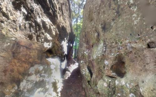 Narrow passage between two large rock formations, with greenery visible in the background.