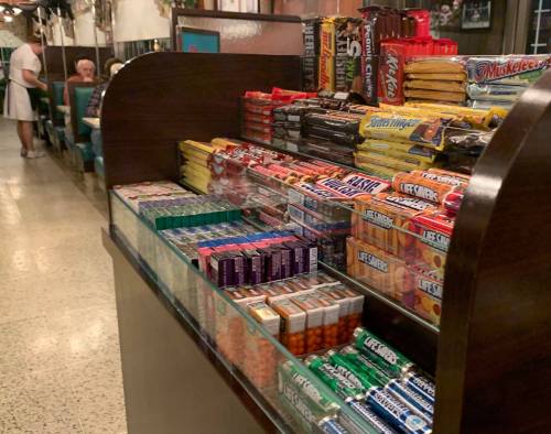 A display of colorful candy and snacks in a retro diner, with patrons seated in the background.