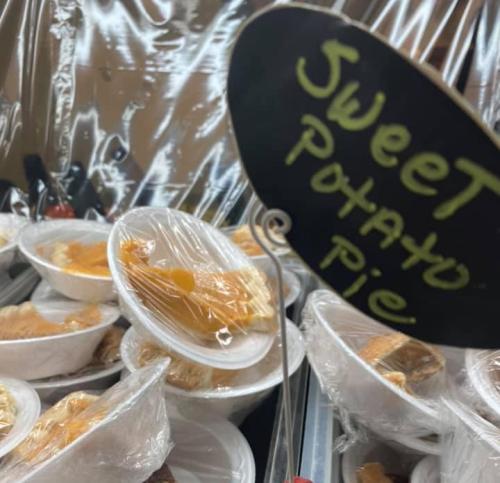 Containers of sweet potato pie covered with plastic wrap, displayed at a food stall.