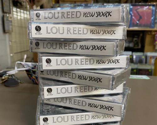 A stack of cassette tapes labeled "Lou Reed New York" on a table in a music store.