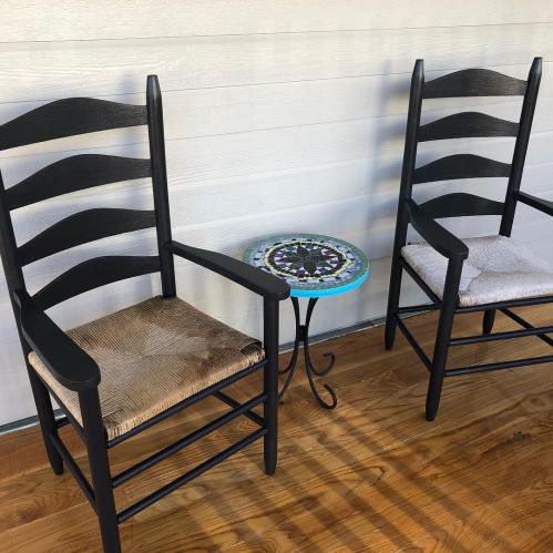 Two black rocking chairs with woven seats beside a small, colorful mosaic table on a wooden floor.