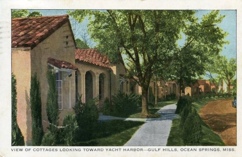 A scenic view of cottages along a path, with trees and a yacht harbor in the background, Gulf Hills, Ocean Springs, Miss.