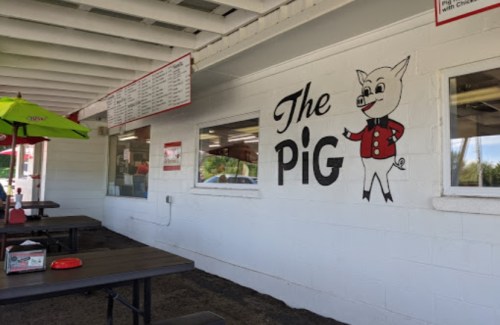 A restaurant exterior featuring a cartoon pig mascot and a menu board under a covered seating area.