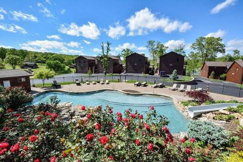 A scenic view of a pool surrounded by flowers, with cabins and trees in the background under a blue sky.