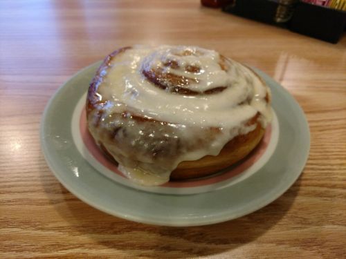 A freshly baked cinnamon roll topped with creamy icing, served on a pastel plate.