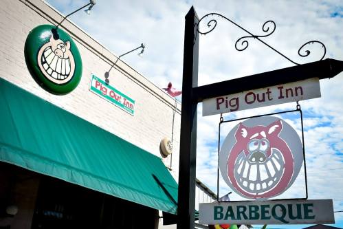 Signage for "Pig Out Inn" featuring a cartoon pig and a green logo, with a barbecue sign below.
